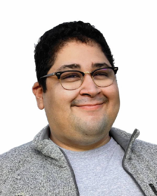 Smiling person with glasses and gray jacket.